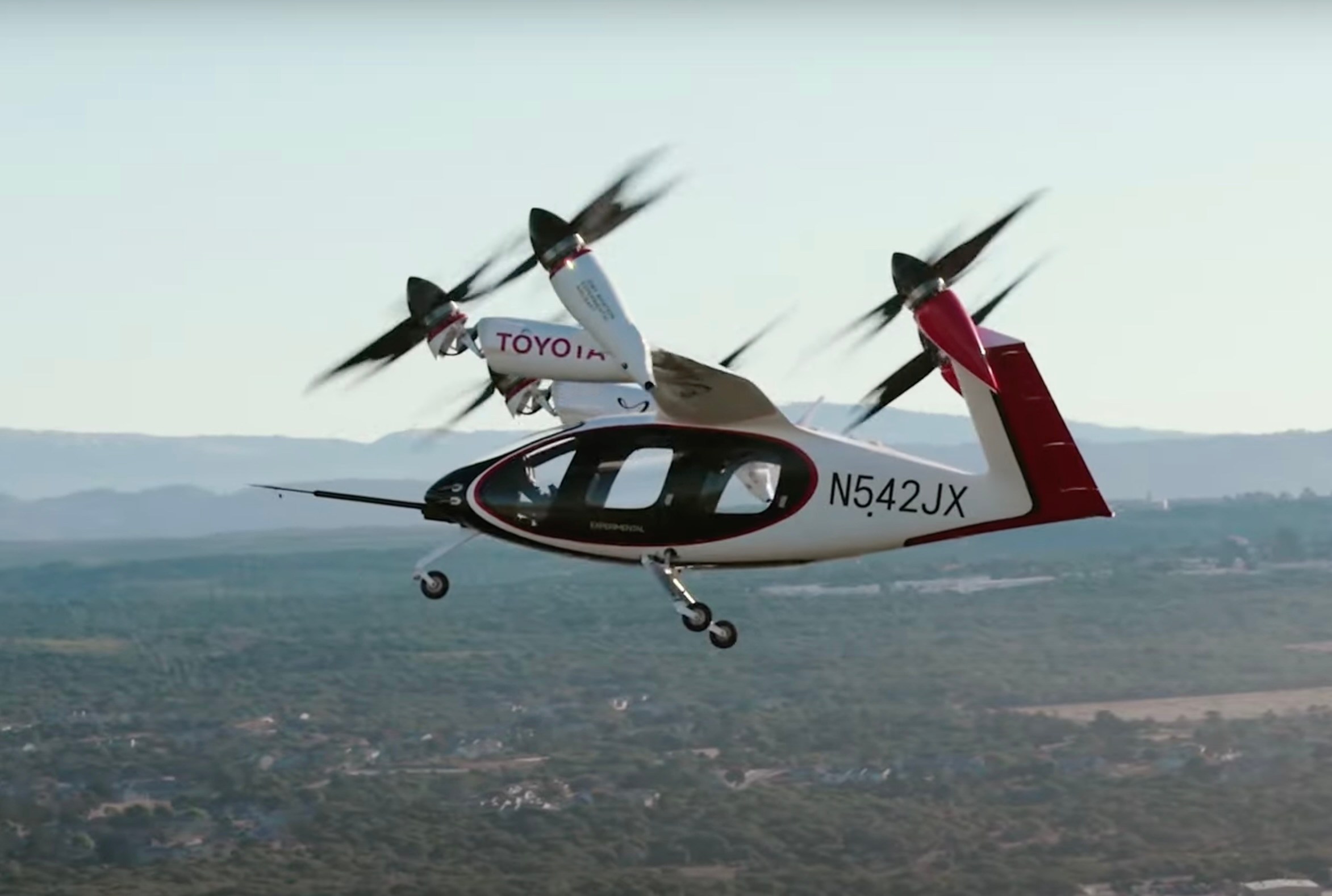 Aircraft in sky with five propellers aiming forward and upward at about 45 degrees, Toyota logo on the wing